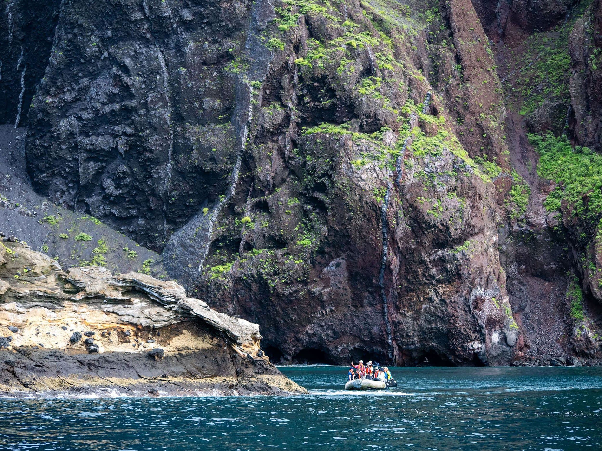 a zodiac ride in front of a high cliff