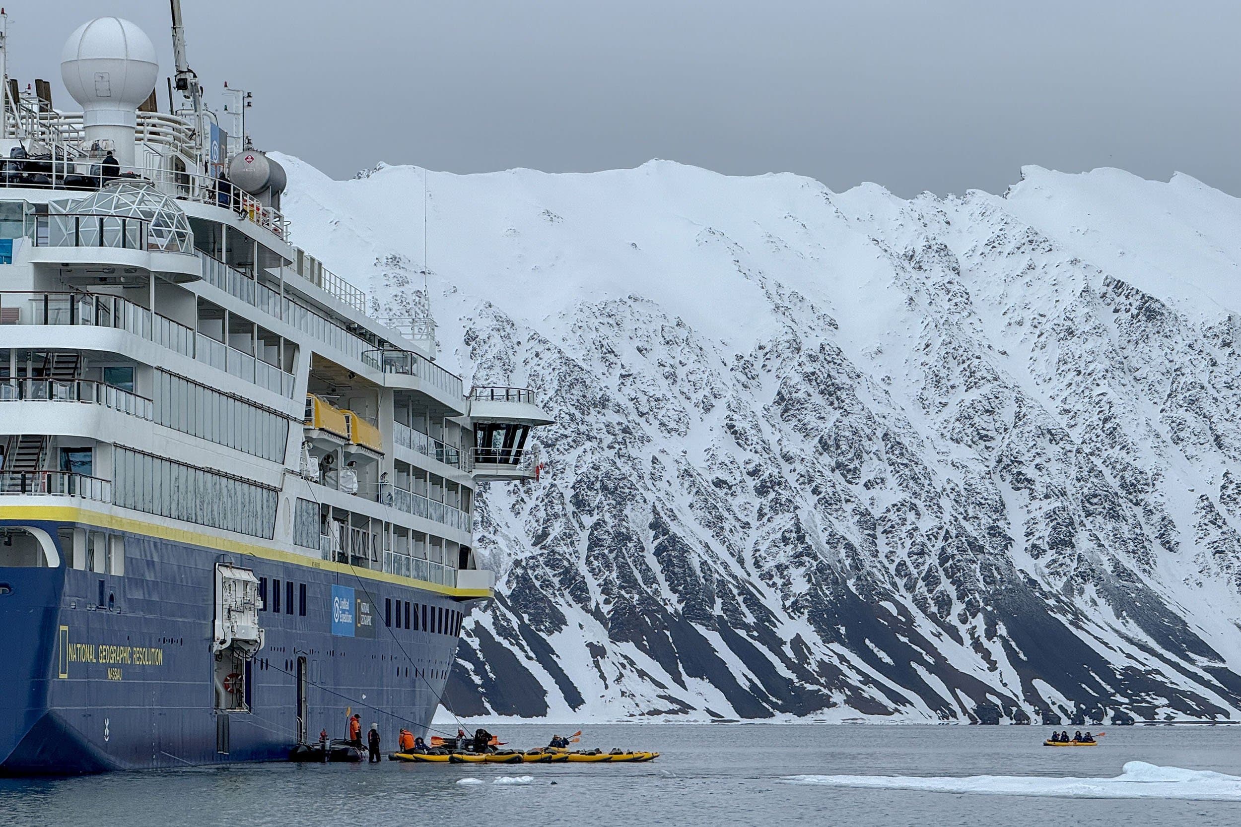 kayaks leave from National Geographic Resolution, with snowy mountains in the background