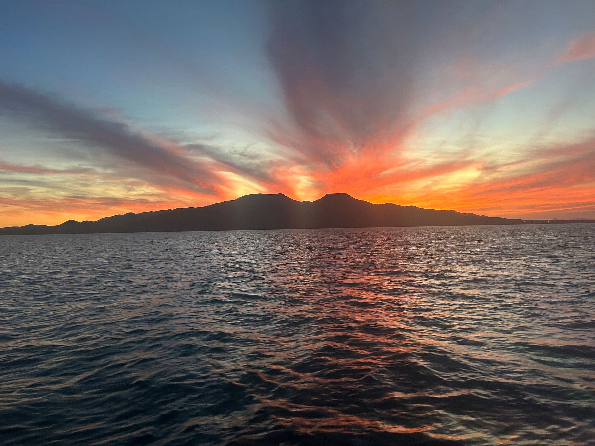 a red and orange sunset behind a mountain and water