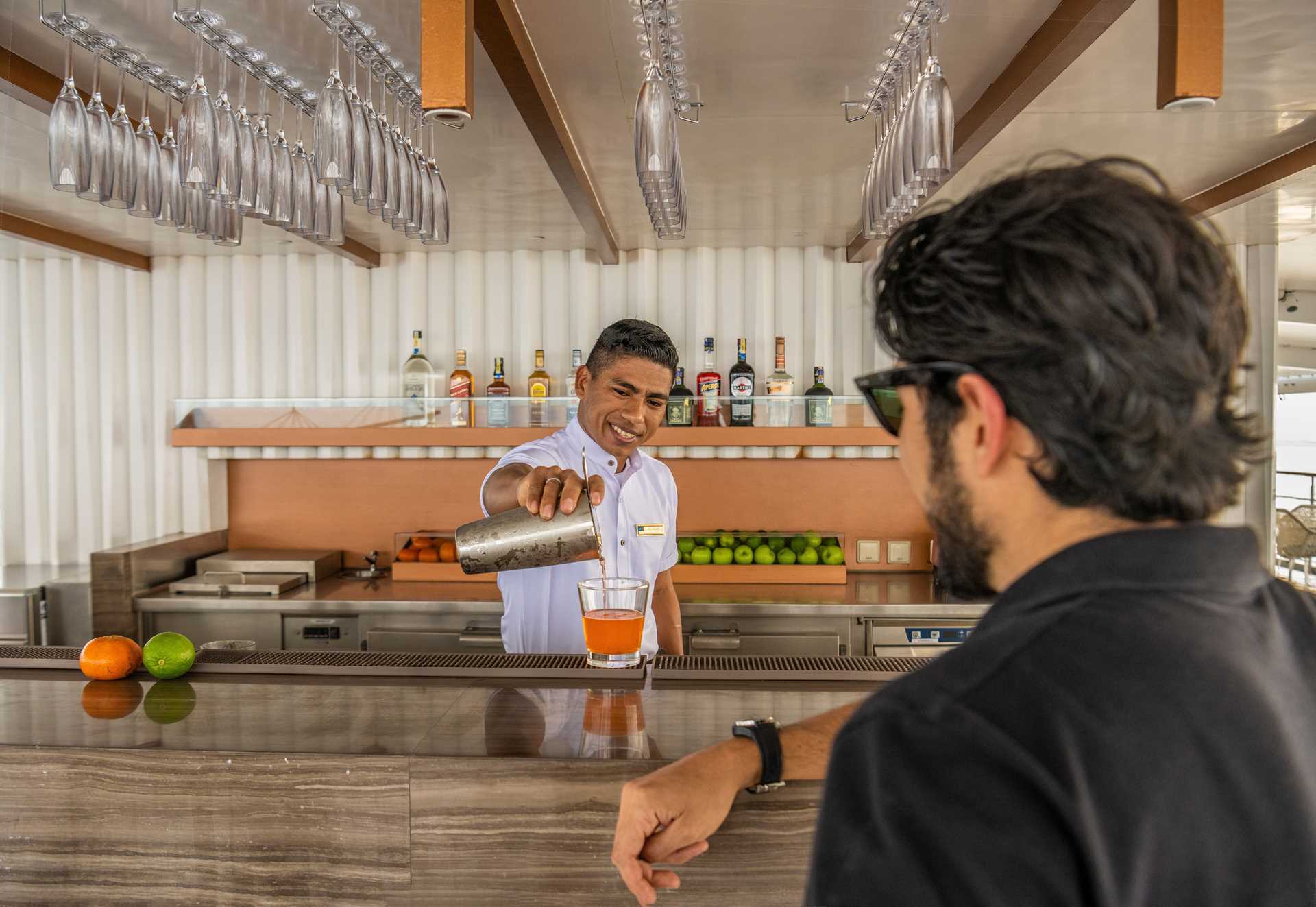 A bartender pours a cocktail for a guest at the observation deck bar on National Geographic Islander II