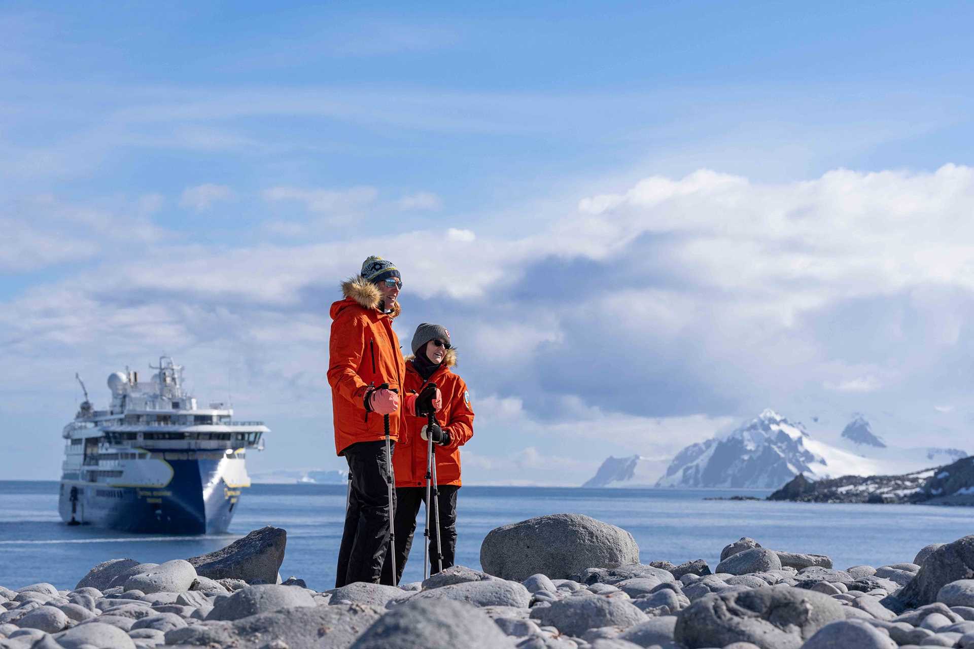 two people stand in front of water in Antarctica, with a ship in the background