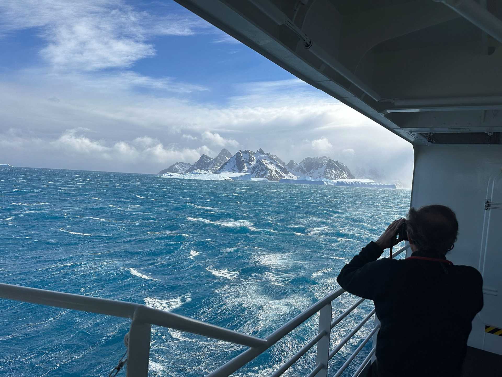 a person stands on the deck of a ship photographing icebergs