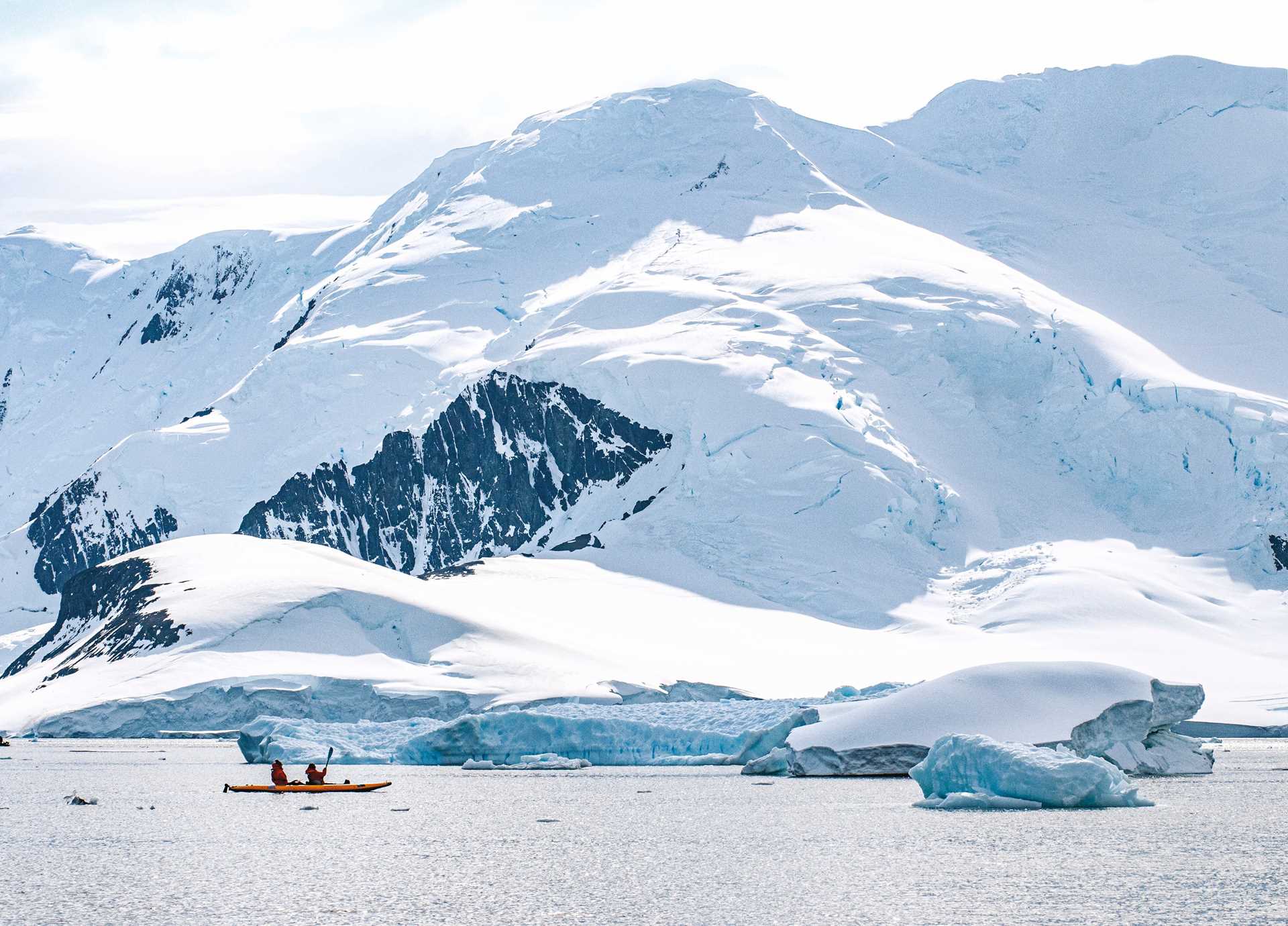 Two kayakers in Antarctica with a mountain in the background.