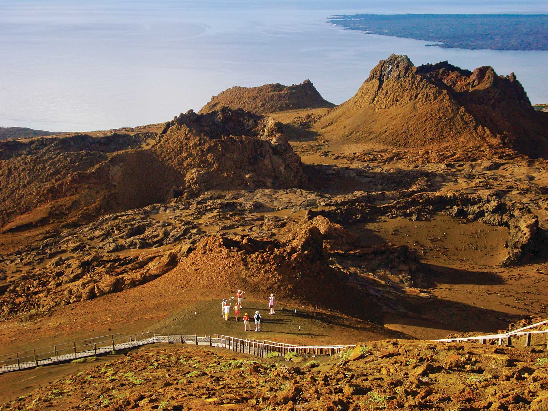 Seven hikers in the distance stand and look out at Bartolomé Island, Galápagos.