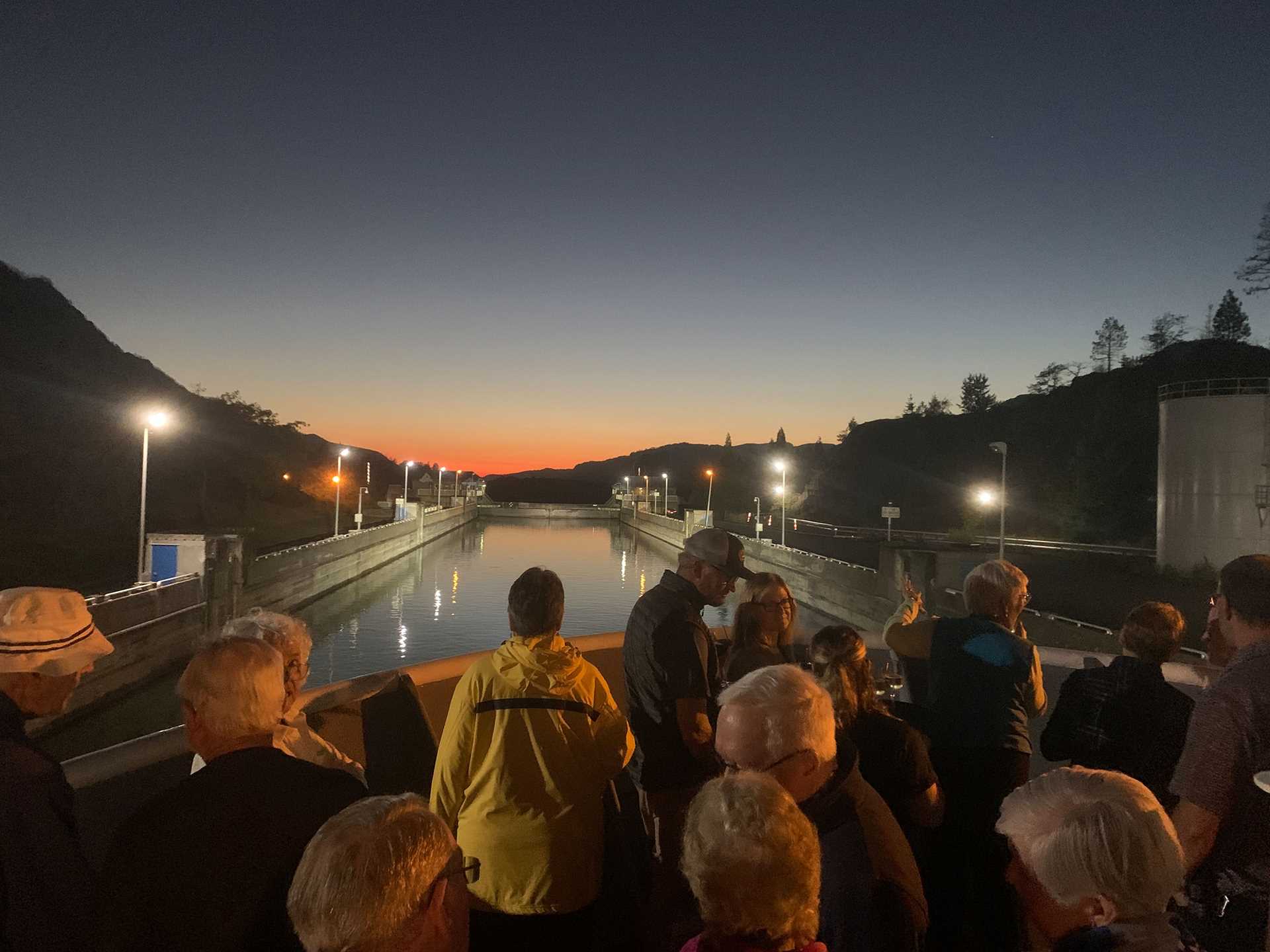 people stand on the bow of a ship in a lock at sunset