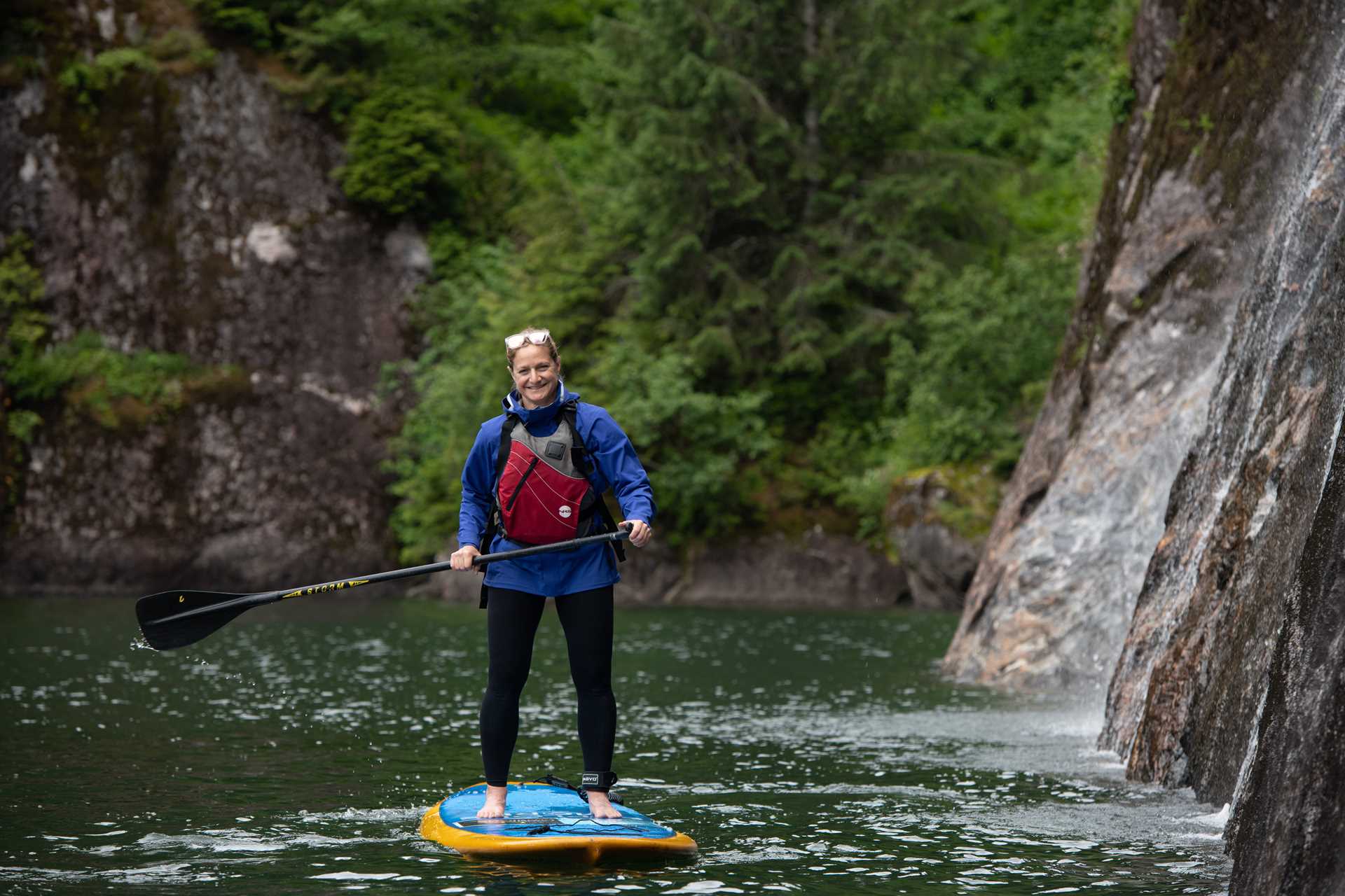 A guest smiles as she explores by Standup Paddleboard, Owl Pass in Rudyerd Bay, Misty Fiords National Monument, Ketchikan, Alaska.