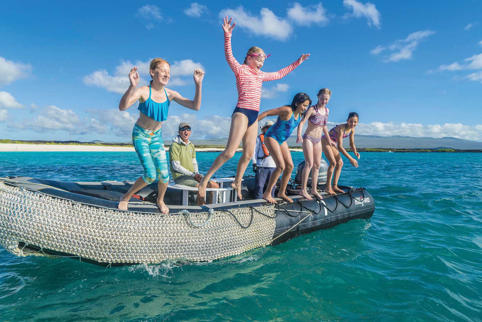 Five young girls jump off the side of a Zodiac into the water.