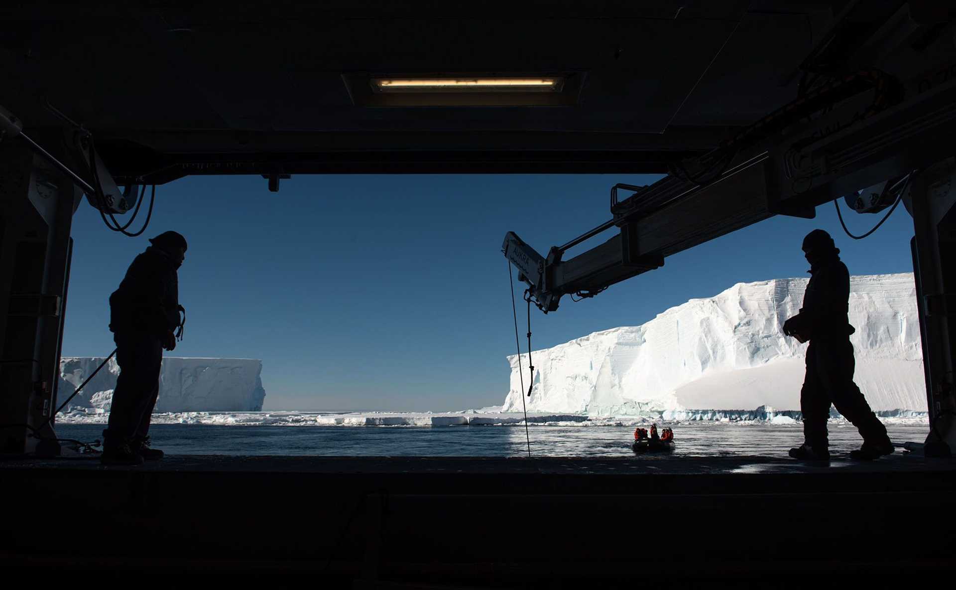 crew silhouetted against an icy ocean with a zodiac coming in